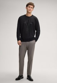 Felpa nera con un motivo grafico testurizzato sul davanti, abbinata a pantaloni chiari grigi con motivo e stivali in pelle nera.