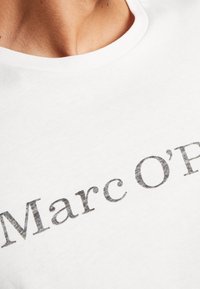 Witte katoenen T-shirt met een ronde hals. Voorzien van een opvallende grijze print van de tekst "Marc O'Polo" over de voorkant in een casual lettertype.