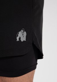 Shorts de sport noirs avec un logo de gorille argenté sur le côté. Tissu doux et léger avec une texture lisse et une coupe décontractée.
