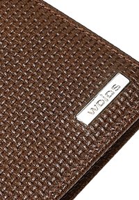 Hnědá peněženka vyrobená z texturovaného materiálu s tkaným vzorem. Na spodním pravém rohu je viditelná stříbrná logo nálepka, švy jsou prošité.