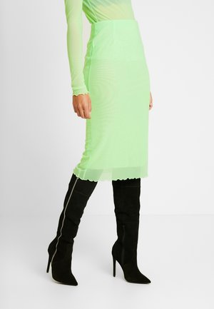 Groene doorschijnende kokerrok met een gegolfde zoom, gecombineerd met zwarte suède stiletto laarzen tot boven de knie met een zijritsdetail.