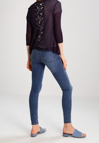 Maglione blu navy con schiena scoperta e pannello in pizzo, jeans skinny blu e sandali blu a fascia. Tessuto leggero con vestibilità rilassata e maniche a tre quarti.