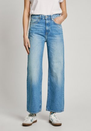 Lichtblauwe wijde jeans gemaakt van denim, met een hoge taille, voorzakken en een schone zoom. Gepaard met witte sneakers.