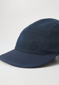 Navy blue cap made of textured fabric with a grid pattern, featuring an embroidered logo and a curved brim.