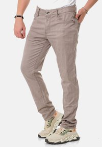 Beige gestreifte Hose aus Baumwolle, mit Slim-Fit-Schnitt und frontalen Taschen. Kombiniert mit beige und grünen Schuhen.
