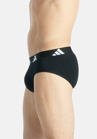 Schwarze Unterhose aus weichem Material mit einem breiten, elastischen Bund, der mit einem weißen Logo in Form von drei Streifen versehen ist. Klassischer Schnitt und Form.