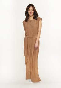 Pleated maxi-tyylinen mekko lämpimässä ruskeassa sävyssä, jossa on lyhyet hihat ja vyötärösiteet. Mekolla on sileä pinta ja virtaava siluetti.