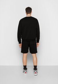 Schwarzer Hoodie und Shorts, aus Baumwolle gefertigt. Der Hoodie hat einen Rundhalsausschnitt und gerippte Bündchen, während die Shorts eine Gesäßtasche haben. Weiße und graue Sneaker.