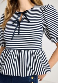 Kvinde iført marineblå og hvide vandrette stribet top med puffede ærmer og to bundne sløjfer ved halsudskæringen.