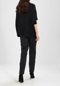 Czarna bluzka z krótkim rękawem o luźnym kroju, zestawiona z wzorzystymi czarnymi spodniami. Modelka w czarnych szpilkach, widoczna z tyłu.