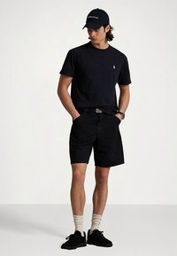 Μαύρο βαμβακερό μπλουζάκι, μαύρα σορτς, μαύρα αθλητικά παπούτσια, λευκές κάλτσες και σκούρο καπέλο. Φέρει μικρό λογότυπο στο μπλουζάκι και το καπέλο.