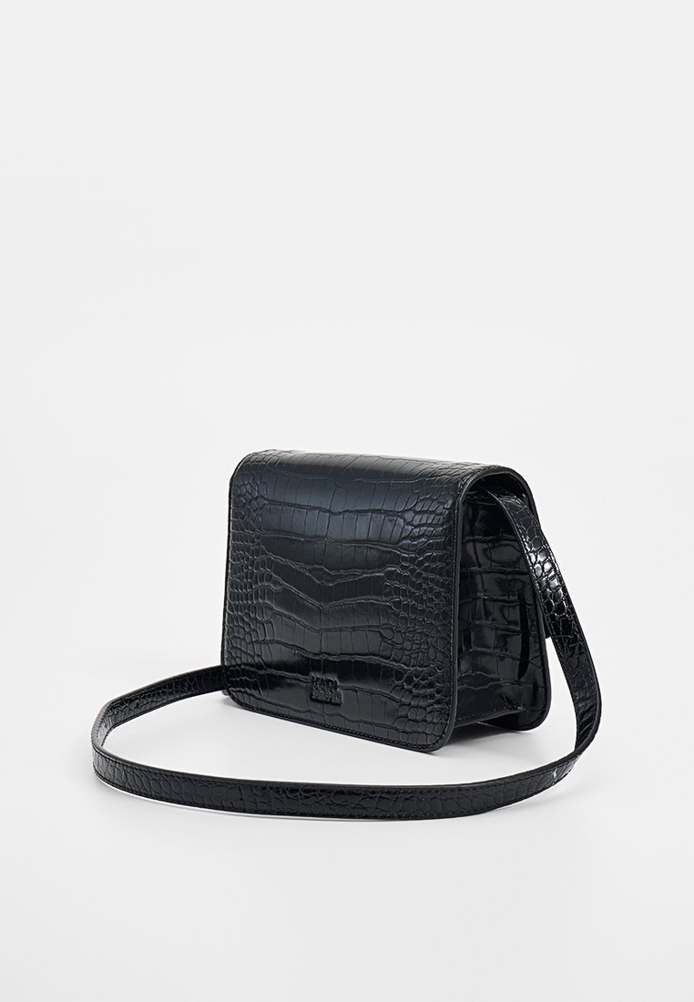Czarna torebka crossbody z sztucznej skóry w motyw krokodyla, z klapką i regulowanym paskiem, na neutralnym tle.