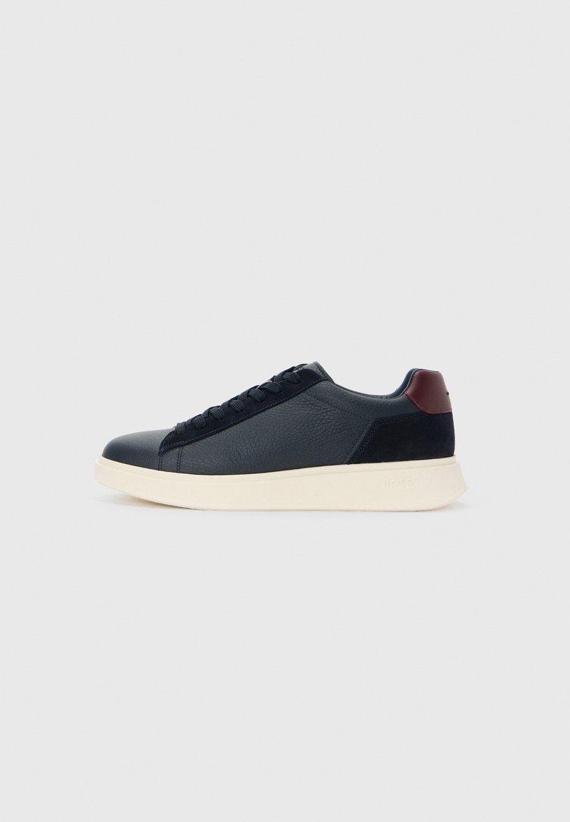 Baskets basses noires à lacets avec avant en cuir texturé, talon en daim, languette de talon bordeaux et semelle épaisse blanc cassé sur fond clair.