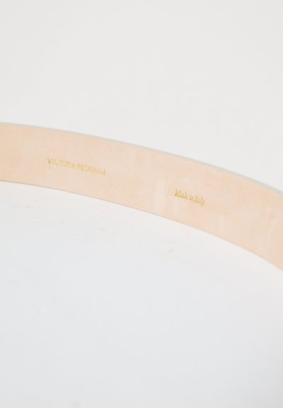 Læderrem med en glat, naturlig finish. Præget tekst: "Victoria Beckham" og "Made in Italy" i guldfolie. Neutral farve.