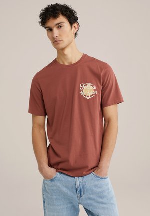 Roodkleurig katoen t-shirt met een ronde borstafbeelding waarop "Follow the Sun" in lichtbeige tekst staat. Korte mouwen, losse pasvorm.