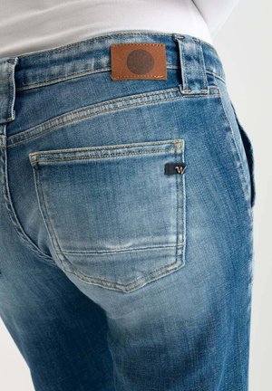 Jean en denim bleu avec une finition délavée, featuring une petite étiquette en cuir marron à la taille et un petit logo sur la poche arrière.