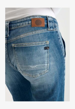 Blauwe denim jeans met een vervaagde afwerking, met een bruine leren patch op de taille en een klein logo op de achterzak.