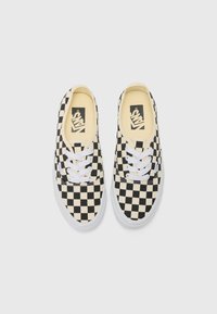 Para czarno-białych trampków Vans w kratkę, z białymi sznurówkami i beżowymi wkładkami, widziana z góry na białym tle.