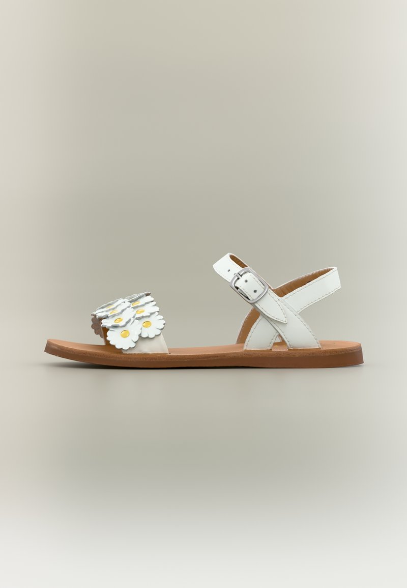 Λευκό επίπεδο σανδάλι με καφέ σόλα, πόρπη λουριού στον αστράγαλο και λουρί στο μπροστινό μέρος διακοσμημένο με στρωματοποιημένα λευκά λουλούδια με κίτρινα κέντρα.