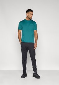 Τυρκουάζ αθλητική μπλούζα, εφαρμοστή γραμμή, σε συνδυασμό με μαύρο παντελόνι με στενή γραμμή και λευκά λογότυπα. Φορώντας μαύρα αθλητικά παπούτσια.