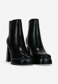 Botines de cuero negro con acabado brillante, punta redondeada, tacón alto de bloque y cremallera lateral para facilitar su uso.