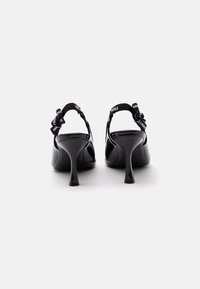 Ζευγάρι μαύρα ψηλοτάκουνα παπούτσια slingback με κυρτά τακούνια και υφασμάτινα λουριά με λογότυπο, σε λευκό φόντο, από πίσω.