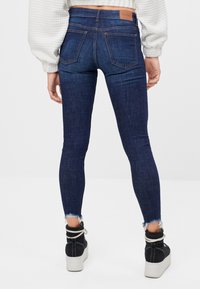 Mörkblå jeans med smal passform och hög midja, med en läderetikett bak och fransad fåll. Kombinationen med svarta platåstövlar.