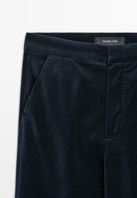 Gros plan sur un pantalon en velours bleu marine foncé avec des poches latérales et une étiquette à la taille indiquant Massimo Dutti.