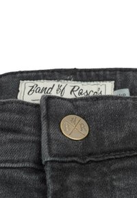 Svarta denimbyxor med en mässingsknapp som har "B/R" ingraverat. Etiketten säger "Band of Rascal's." Slät textur med en hållbar design.