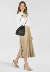 Borsa a secchiello nera con motivo di testo bianco, indossata a tracolla. Modella in camicia bianca e gonna pieghettata beige, abbinata a scarpe con tacco nude.