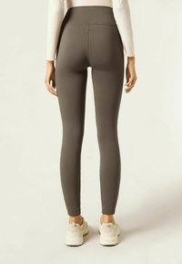 Leggings taille haute, ajustés, en tissu gris foncé, dotés d'un design sans coutures et d'un style minimaliste, associés à des baskets de couleur claire.