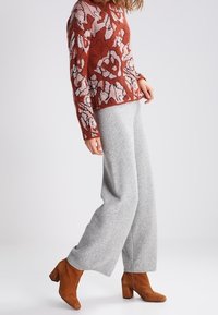 Rød- og pinkfarvet strikket sweater med blomsterprint kombineret med grå bukser med vide ben. Brune ankelstøvler med hæl fuldender outfittet.