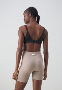 Svart stoff-bh med justerbare stropper og krok-lukking. Beige ribbede shorts med høy midje og diskret merke på baksiden.
