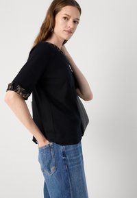 Haut décontracté noir avec des poignets roulés imprimé léopard, col rond et coupe décontractée, associé à un jean en denim bleu. Design simple.