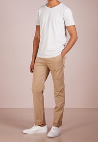 Bílé bavlněné tričko, béžové bavlněné chinos kalhoty a bílé tenisky. Chinos mají rovný střih, tričko má kulatý výstřih a krátké rukávy.