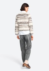 Maglione lavorato a maglia con righe orizzontali in beige, marrone e grigio; scollatura rotonda; abbinato a pantaloni grigi a sigaretta e zoccoli con tacco in legno.