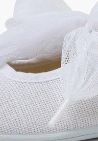 Zapato de tela blanca con textura tejida, adornado con un lazo de encaje y un diseño suave y ligero. Bordes lisos y detalles sutiles.