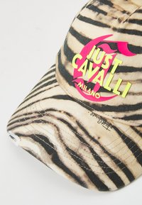 Casquette avec une base beige ornée de rayures noires de tigre, un logo "Just Cavalli Milano" en rose et jaune fluo, et des détails de couture visibles.