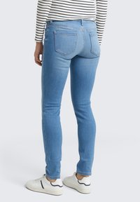 Jeans ajustados de color azul claro con un diseño de cinco bolsillos. Presentan costuras sutiles y una cintura de altura media. Llevados con zapatillas blancas.