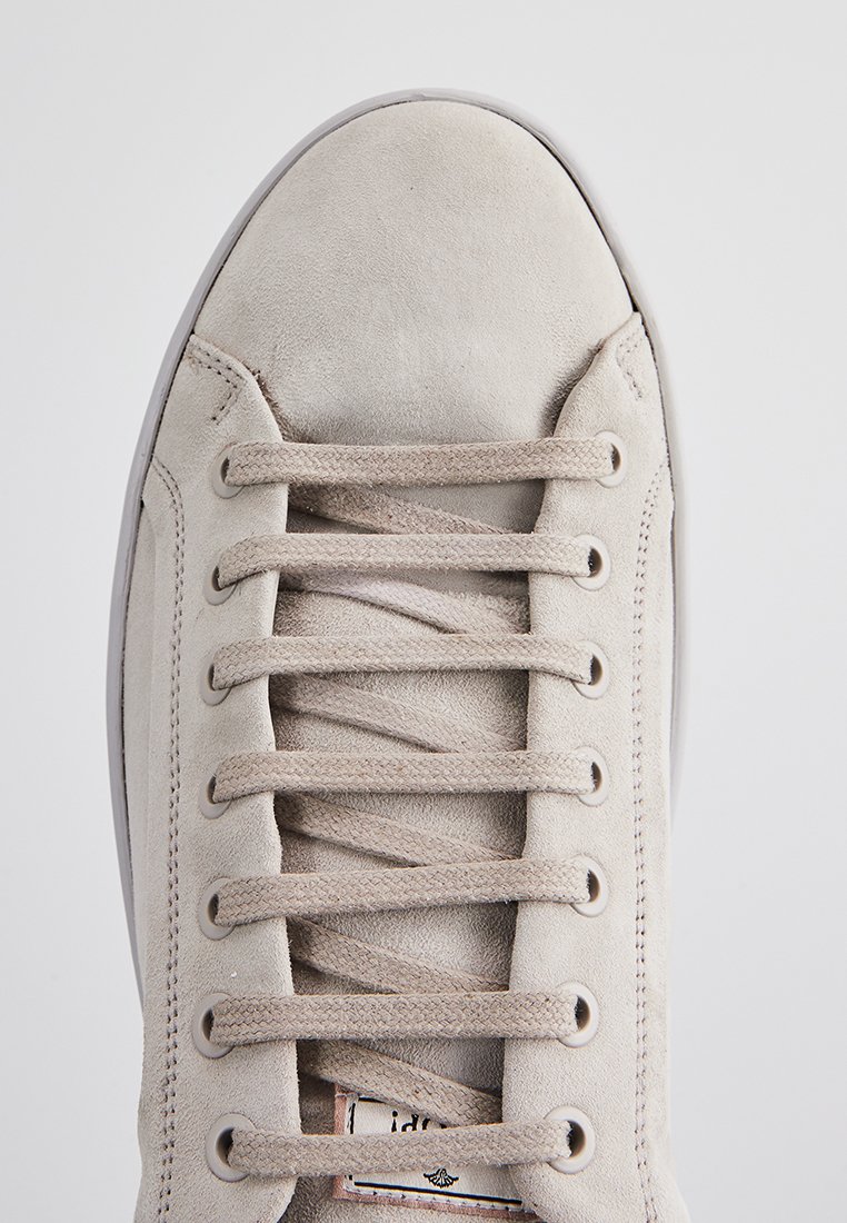 Beżowe zamszowe sneakersy z zaokrąglonym noskiem, sześcioma oczkami na sznurowadła i gładką tekstylną podeszwą. Zawierają małe logo obok języka.