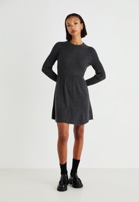 Robe tricotée côtelée gris foncé avec des manches longues, un corsage ajusté et une jupe évasée. Portée avec des chaussettes noires et des chaussures à plateforme.