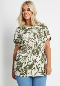 Top a fiori verde e bianco con maniche corte, texture a coste, scollatura tonda e spacchi laterali, abbinato a jeans blu.