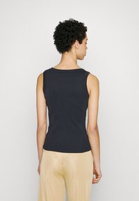 Svart ermeløs tank topp med rund hals, tettsittende design og myk bomullsmateriale, kombinert med beige bukser. Ingen bemerkelsesverdige mønstre eller aksenter.