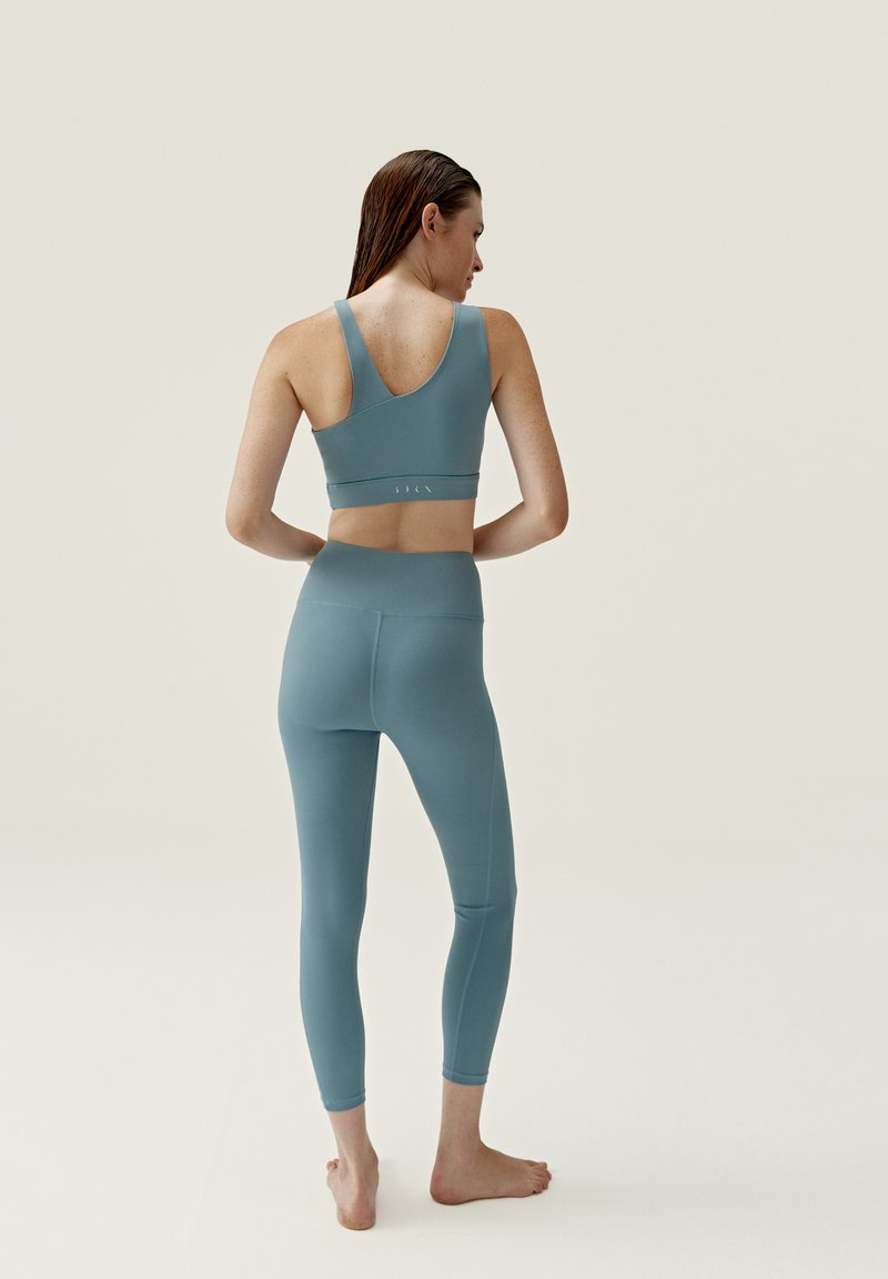 Conjunto de leggings de cintura alta y sujetador deportivo en azul suave, fabricado en un tejido liso y elástico. Presenta un escote en la espalda y detalles de costura sutiles.
