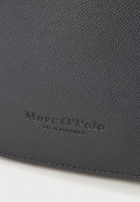 Tmavě šedá texturovaná kožená peněženka s embosovaným logem "Marc O'Polo" s jasným písmem a hladkými okraji. Jednoduchý design, bez dalších akcentů.