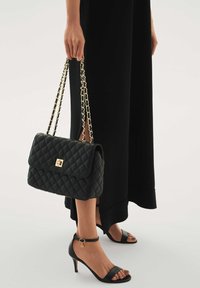 Mustast tikandiga käekott ahela rihmaga, kuldse pandla detailiga. Kandmiseks pika musta kleidi ja mustade kontsakingadega.