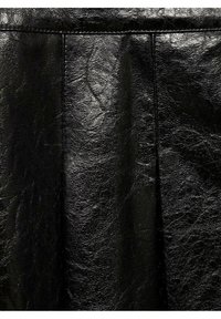 Gros plan sur un tissu en cuir noir brillant avec des plis visibles et des lignes de couture verticales.