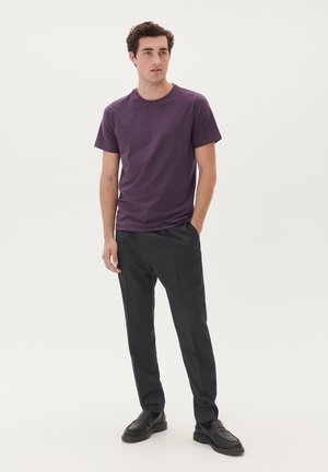 Lila Baumwoll-T-Shirt mit rundem Ausschnitt, kombiniert mit schwarzen Hosen und schwarzen Slippern. Einfaches Design und figurbetonte Silhouette.
