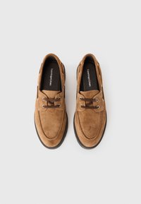 Une paire de chaussures décontractées en cuir suédé marron à lacets, avec des semelles foncées et des semelles intérieures noires, étiquetées "Chaussures Copenhague" sur fond blanc.