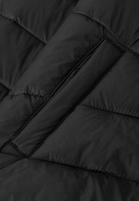 Dettaglio di un giubbotto in piuma nero, caratterizzato da sezioni trapuntate, una texture liscia e una tasca con zip nascosta. Design leggero e isolato.
